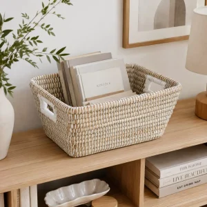 Handmade seagrass storage basket holding books and magazines on a wooden shelf.